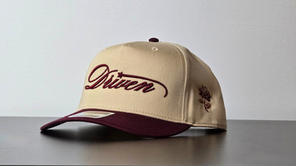 Beige cap with maroon brim and embroidered text on a gray surface