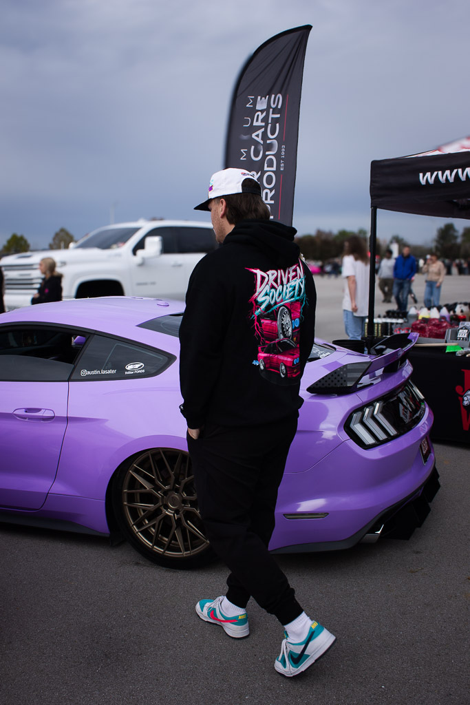 Person walking past a purple car with a visible brand banner in the background