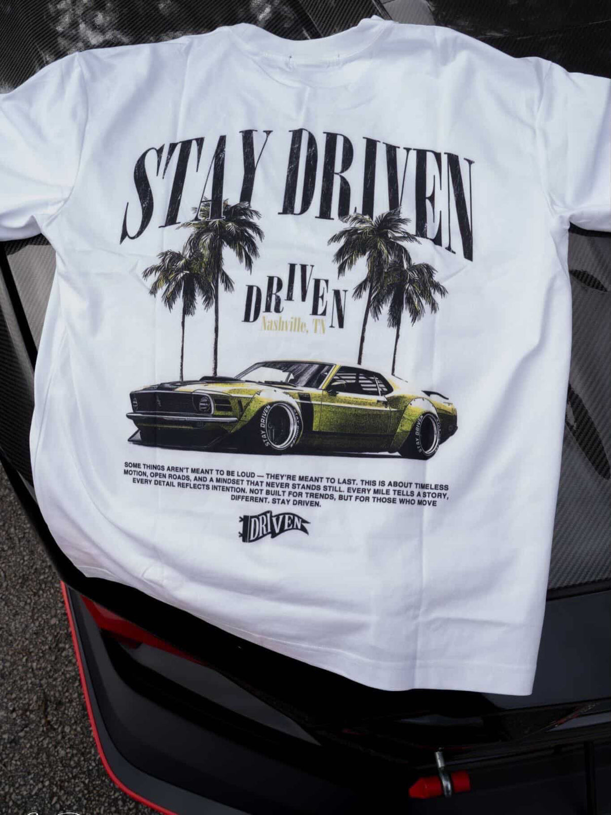 White t-shirt with car graphic and 'Stay Driven' text on a vehicle's rear window.
