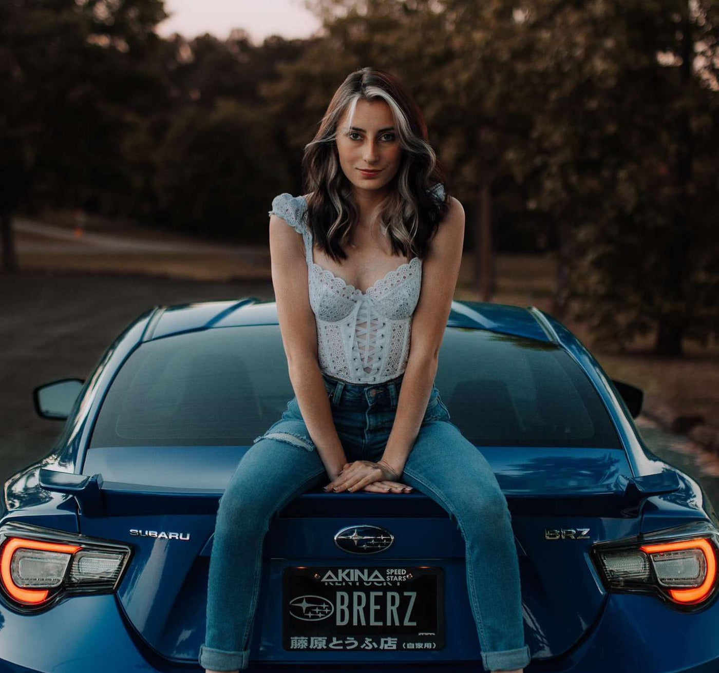 Woman sitting on a blue Subaru car with a blurred background