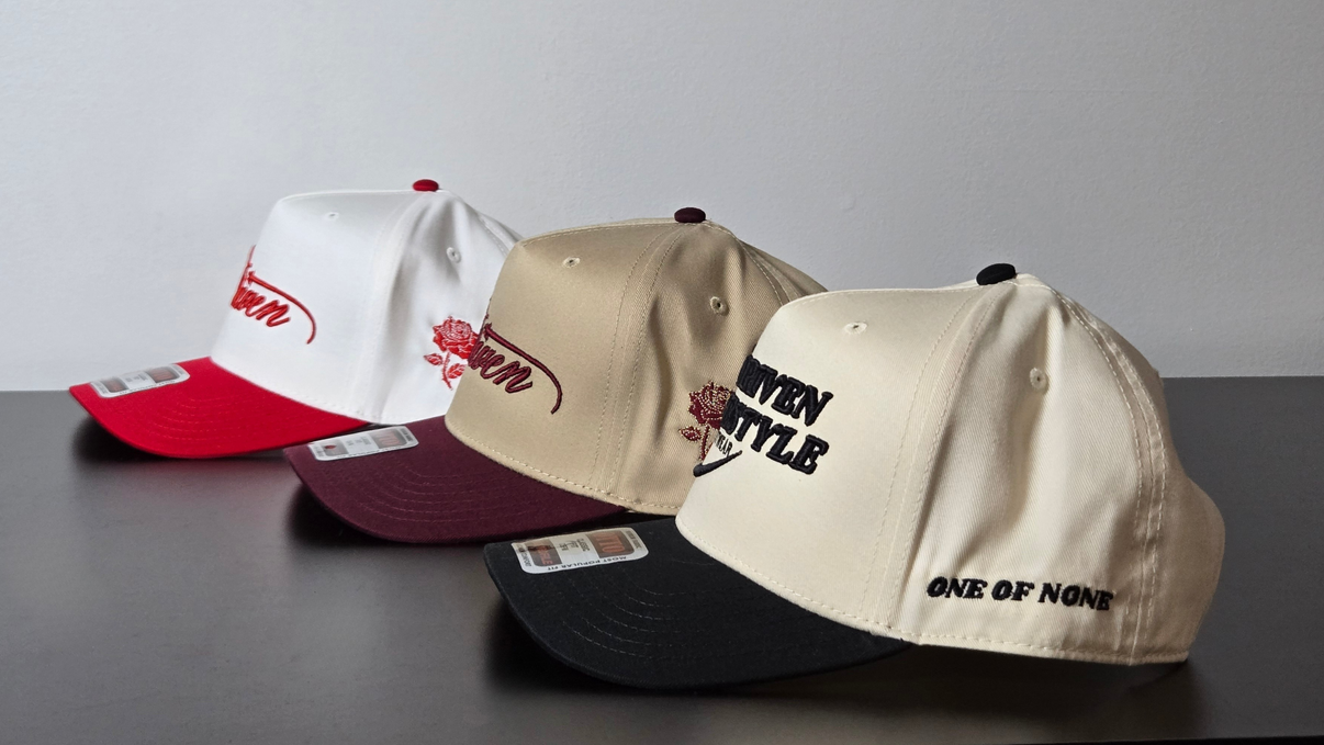 Three baseball caps with different designs and text on a gray surface.