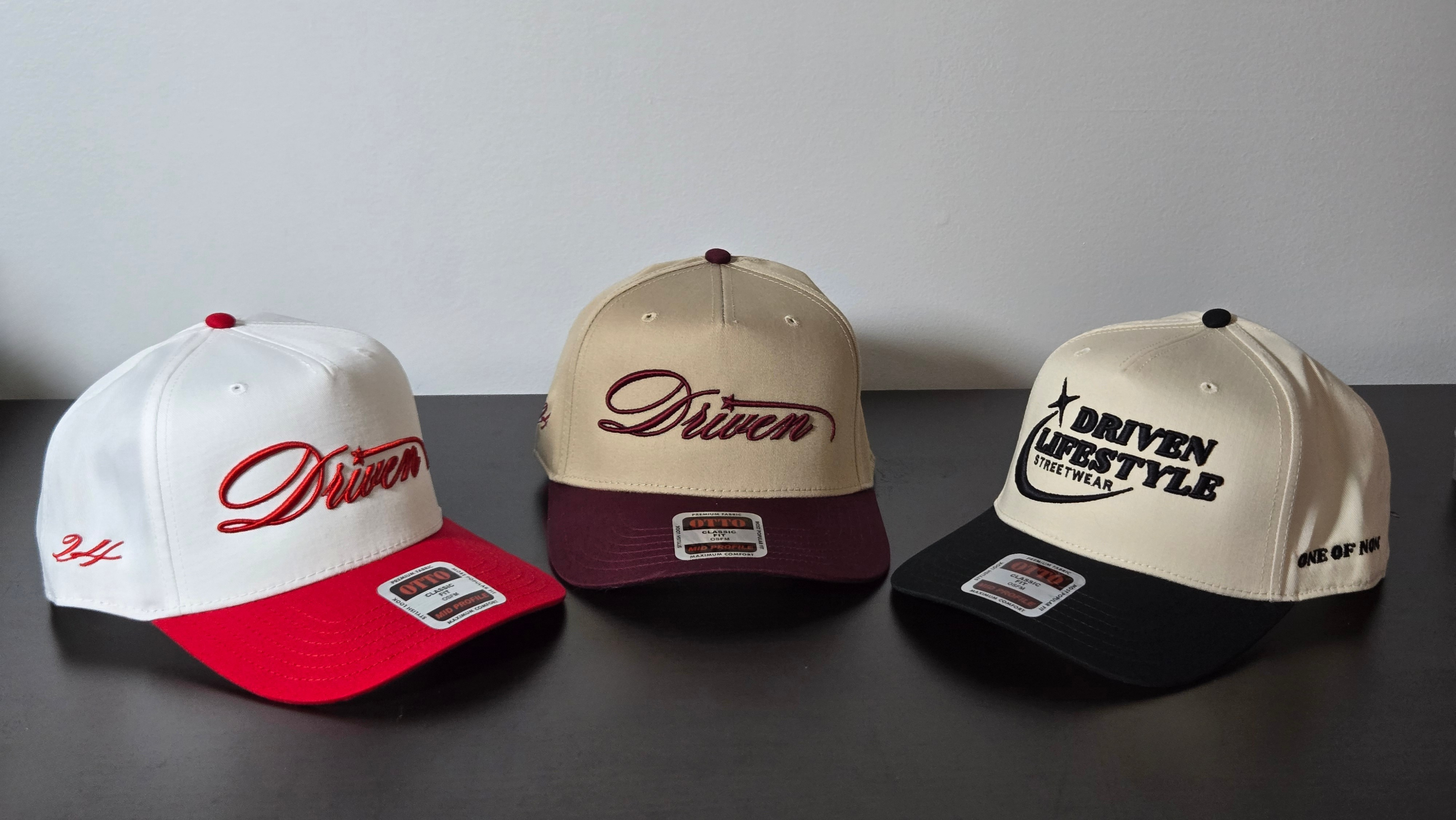 Three baseball caps with 'Driven' branding on a dark surface.