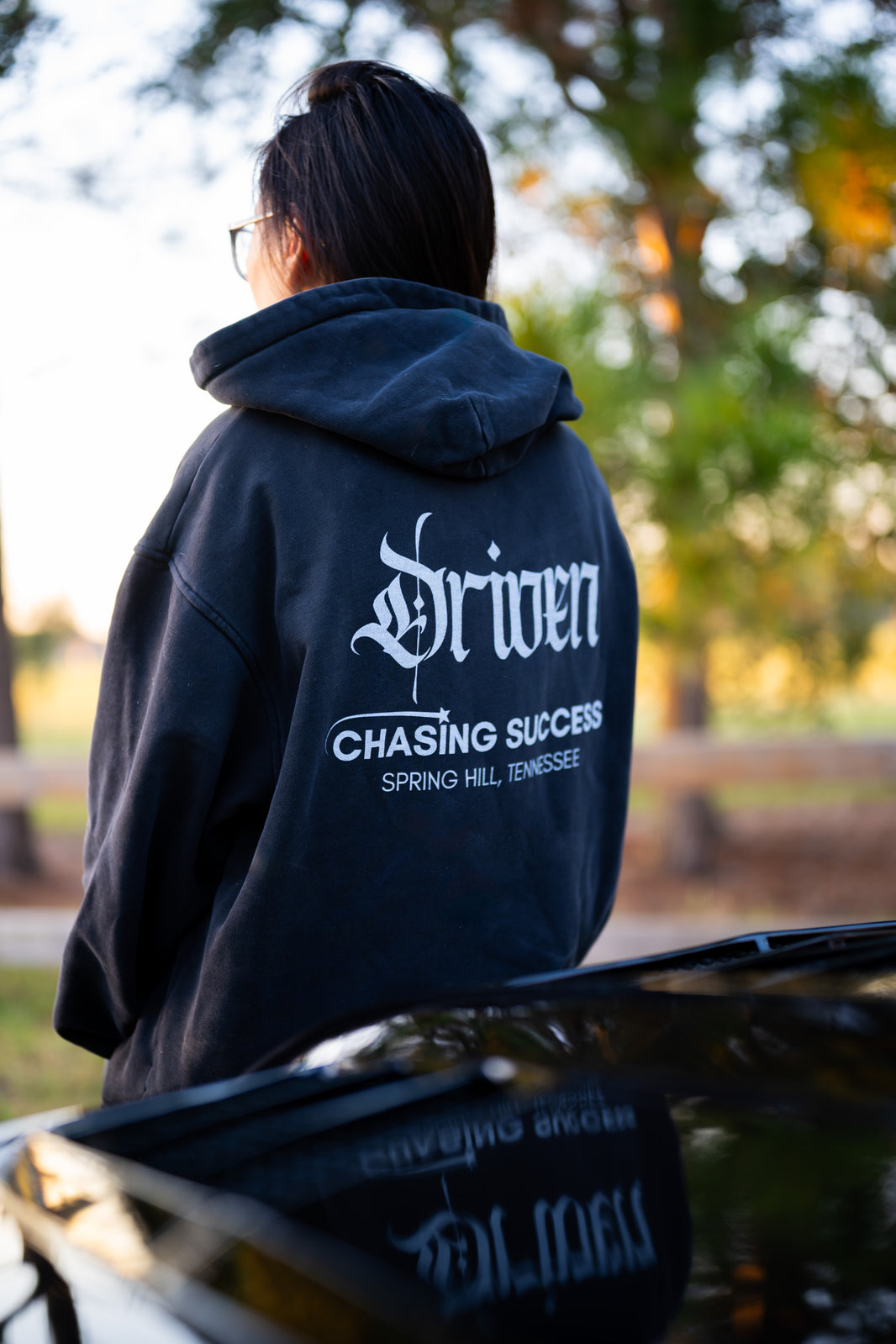 Person wearing a black hoodie with 'Driven' 'chasing success spring hill, tennessee' branding outdoors