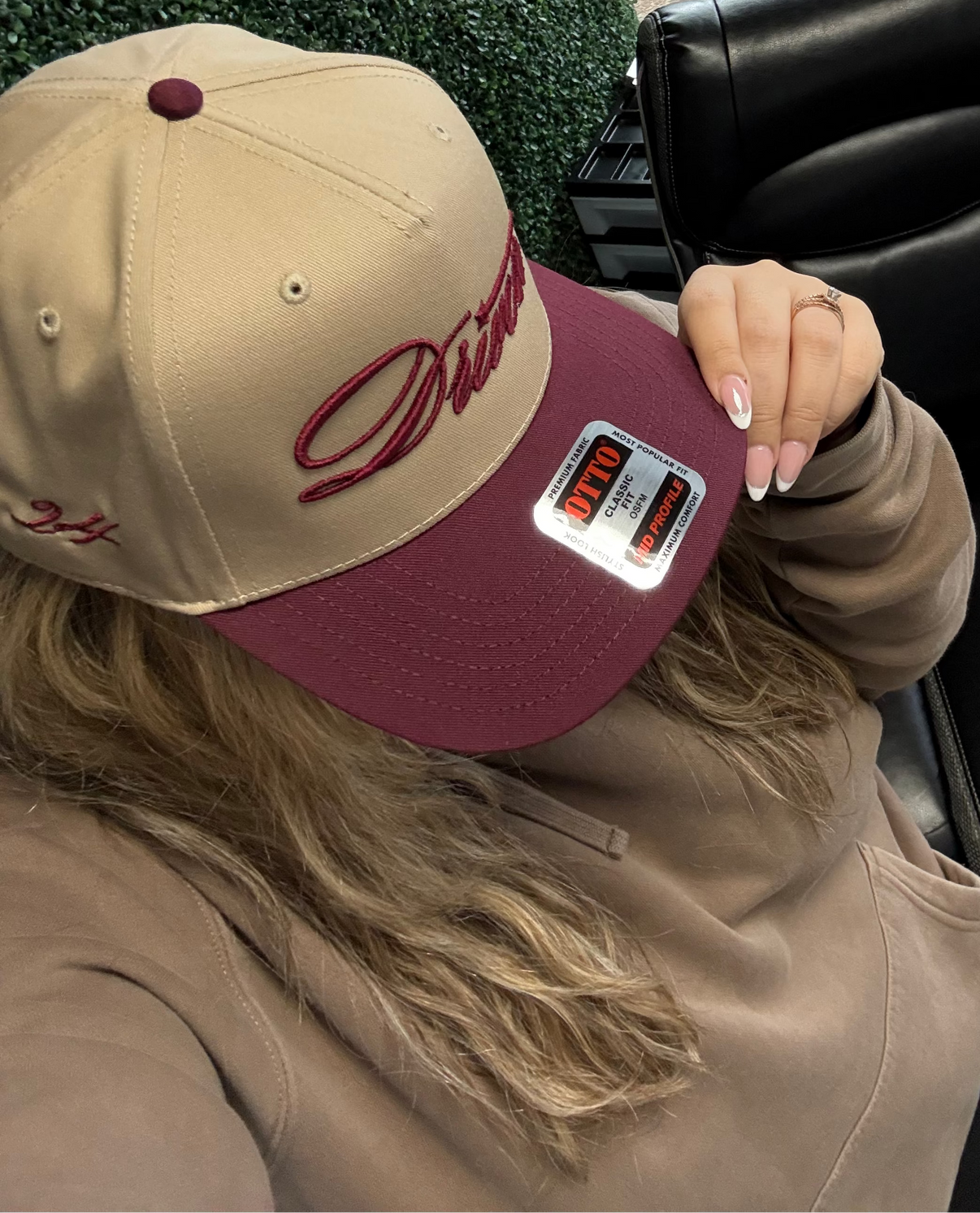 Person wearing a beige and maroon cap with a logo, sitting inside a vehicle.