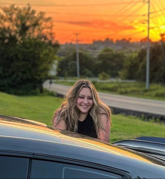 Woman sitting in a car with a sunset in the background