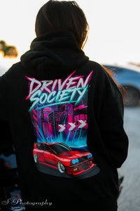 Person wearing a hoodie with 'Driven Society' design on the back with a graphic red widebody bmw e30 and graphic colorful cityscape design