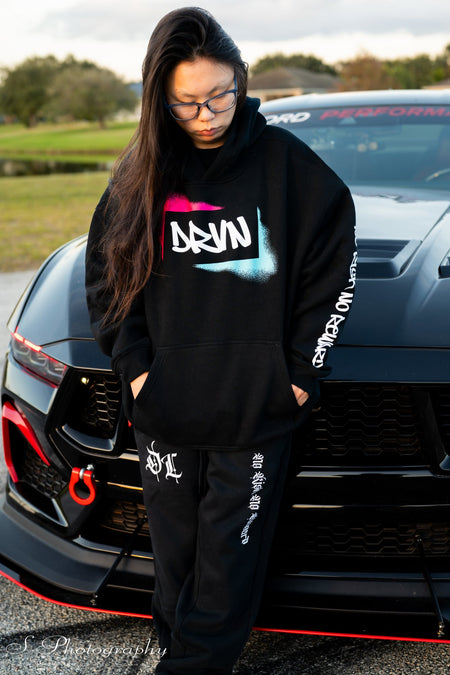 Person wearing a black hoodie with visible branding in front of a car