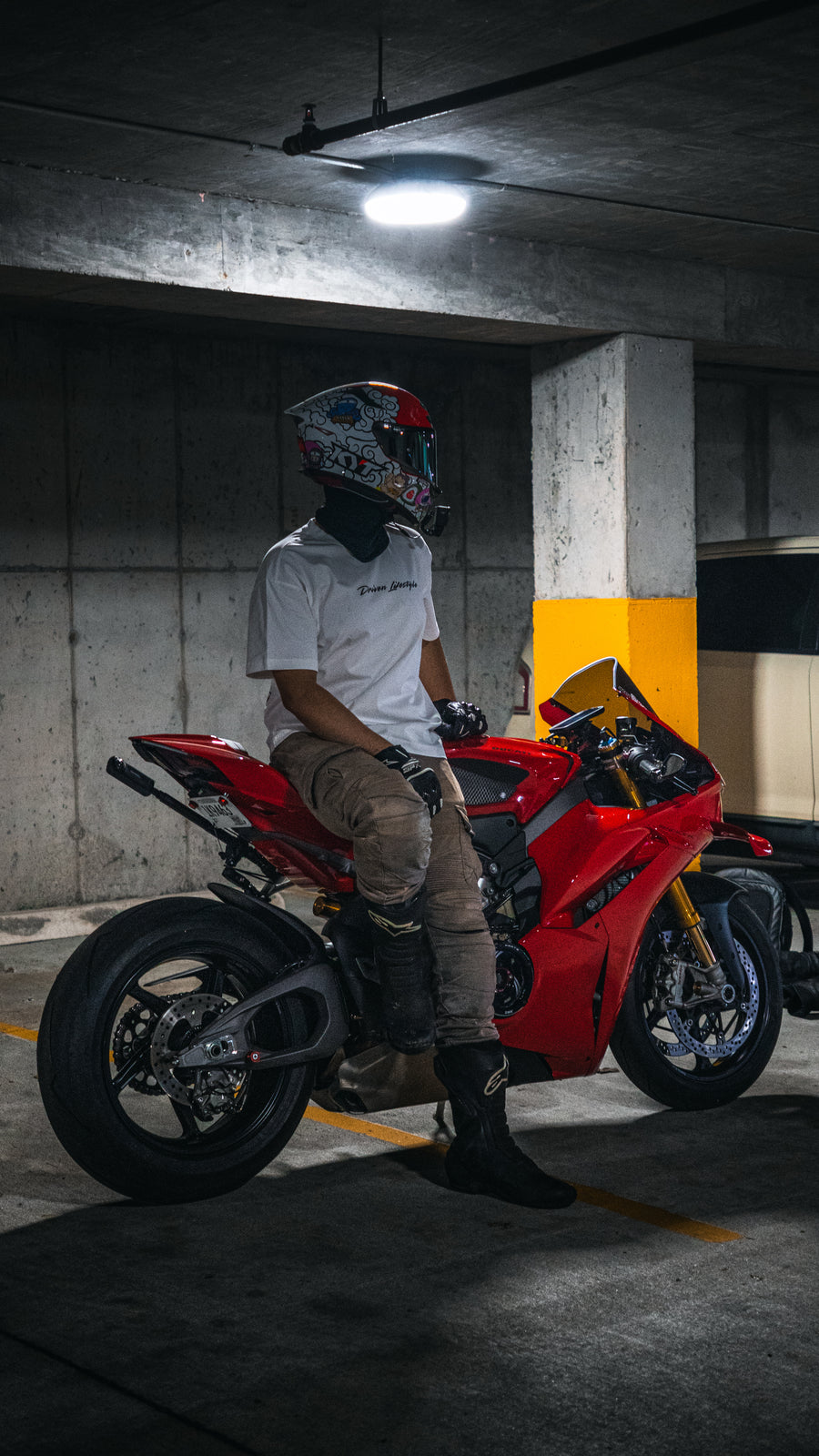 Load video: Video of a biker on a red Ducati wearing a white Driven Lifestyle t-shirt, and model posing on the bike